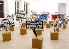 many signs are placed on cardboard boxes in an empty room with white walls and windows