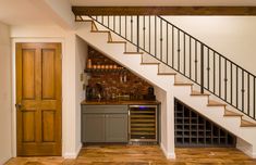 a wine rack under the stairs in a home bar with wooden floors and white walls