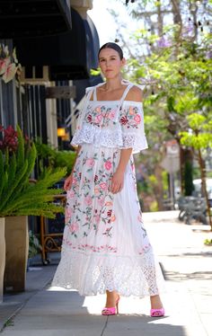 a woman is standing on the sidewalk wearing a white dress with pink flowers and lace