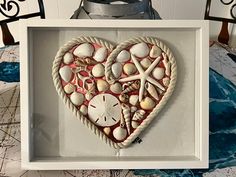 a heart made out of seashells in a white frame on top of a table