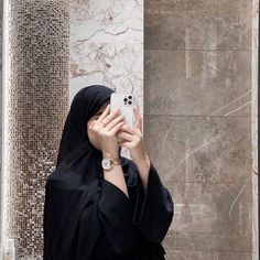 a woman wearing a black hijab taking a selfie with her cell phone