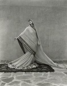 an old fashion photo of a woman in a white dress sitting on a rug with her arms outstretched