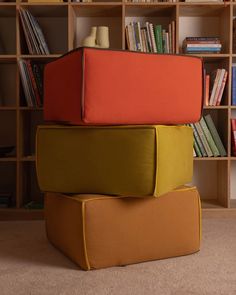 three different colored pillows stacked on top of each other in front of bookshelves