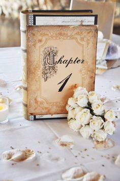 a table topped with white flowers and an old book next to a candle on top of it