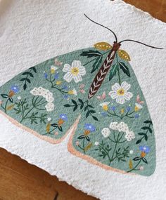 a close up of an embroidered butterfly on a piece of cloth with flowers and leaves