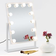 a mirror with lights on it next to a vase and flower in the foreground