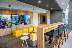 an office lobby with yellow and black chairs, tables and televisions on the wall