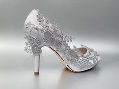 a pair of white wedding shoes with flowers and leaves on the heels are shown in front of a gray background