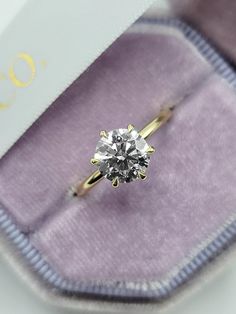 an engagement ring with a diamond in it's gift box on top of a purple velvet bag