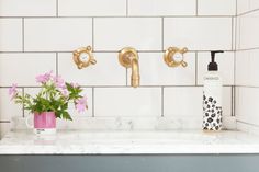 two faucets on the wall above a sink with pink flowers and soap dispenser