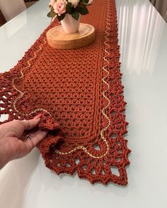 a hand is holding the edge of a crocheted table runner