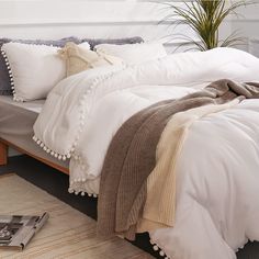 a bed with white comforter and pillows on it next to a plant in a vase