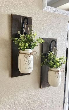 two mason jars are hanging on the wall with plants in them and one is holding scissors