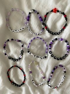 six bracelets with black, white and purple beads are laid out on a bed