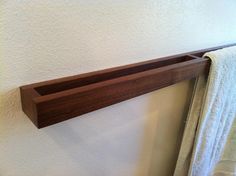 a wooden shelf hanging on the wall next to a towel rack in a room with white walls