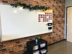 a whiteboard mounted to the side of a brick wall next to a book shelf