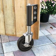 a black and silver dolly with wheels on the ground next to a wooden fence in front of flowers