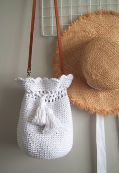 a white crocheted bag hanging on a wall next to a straw hat and basket