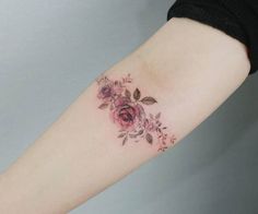 a woman's arm with pink roses on it and leaves around the wrist tattoo