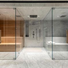 a bathroom with marble walls and flooring, glass partitions to separate the bathtub from the walk in shower area