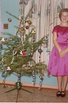 a woman in a pink dress standing next to a christmas tree