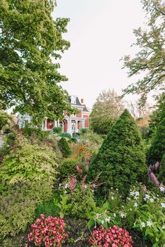 the garden is full of colorful flowers and trees in front of a large white house