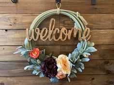 a welcome wreath hanging on a wall with flowers and the word welcome written in wood