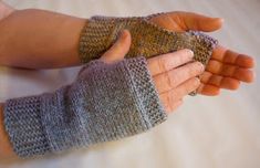 two hands wearing knitted gloves on top of a bed