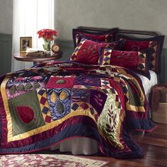 a bed covered in a colorful quilt next to a table with a vase on it