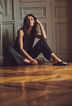 a woman is sitting on the floor with her hands behind her head and looking at the camera