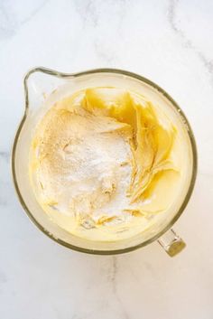 an overhead view of a blender filled with yellow liquid and flour on a marble counter top