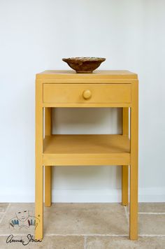 a small yellow table with a bowl on it's top next to a white wall