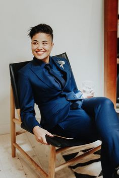 a man in a blue suit sitting on a chair with a wine glass and smiling