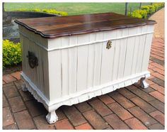 a white chest with wooden top on brick walkway next to flowers and water in the background