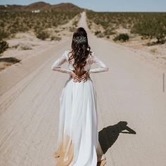 a woman in a white dress walking down a dirt road with her back to the camera