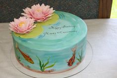 a birthday cake decorated with pink flowers and water lilies on a white tablecloth