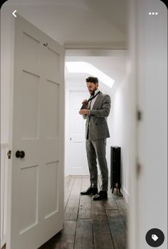 a man standing in front of a white door wearing a suit and looking at his cell phone