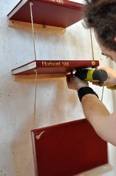 a man is working on some shelves with red and yellow books hanging from it's sides