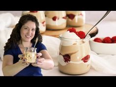 a woman is holding a spoon in front of a jar of desserts with strawberries on top