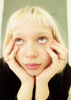 a woman with blonde hair and blue eyes holding her hands to her face while looking at the camera