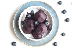 some blueberries are in a white bowl on a plate and scattered with blueberries