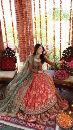 a woman in an orange and green lehenga sitting on a rug with flowers