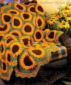 a crocheted sunflower afghan sits on a wicker chair next to flowers