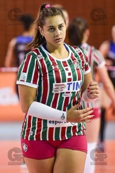 a female volleyball player in red shorts and green striped shirt with her arm wrapped around the waist