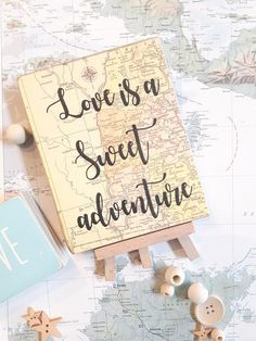 a wooden sign that says love is a sweet adventure next to some buttons on a map