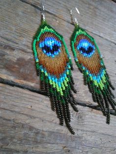 two pairs of beaded earrings with blue and green feathers on them sitting on a wooden surface