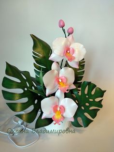 there is a vase with flowers and green leaves on the table next to a cord