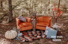 two orange chairs sitting on top of a plaid blanket in the middle of a forest