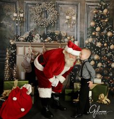 a young boy standing next to santa clause in front of a christmas tree