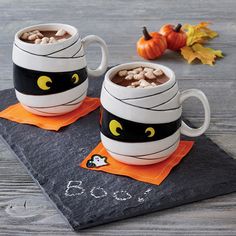 two mugs with halloween decorations on them sitting on top of a napkin next to pumpkins